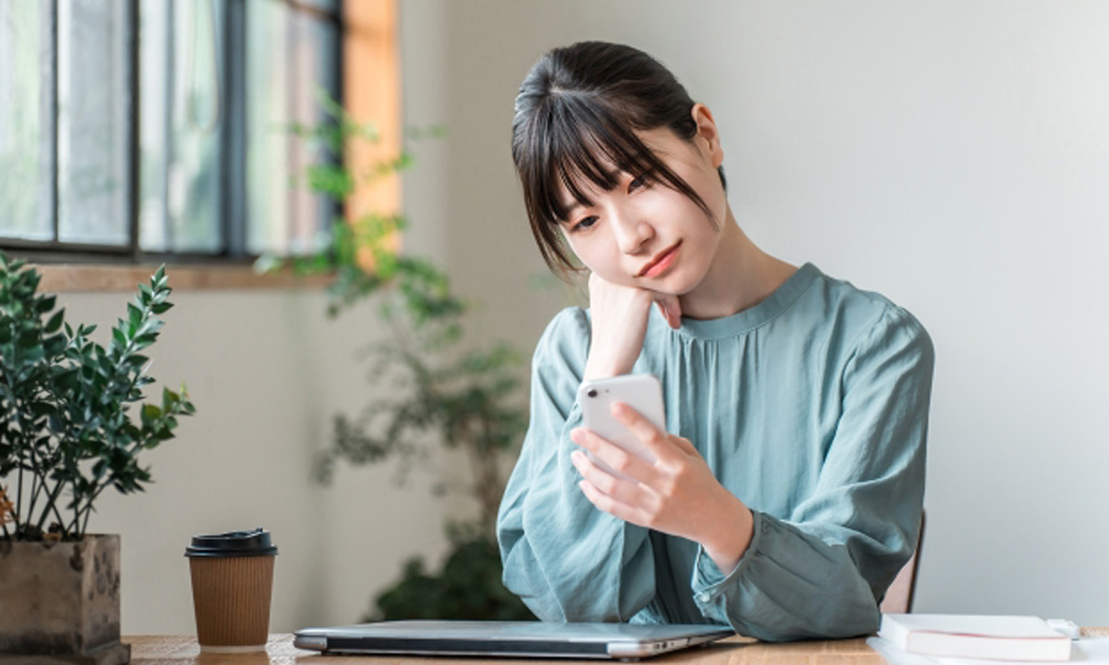 スマホを片手にネット通常で悩んでいる女性のイメージ