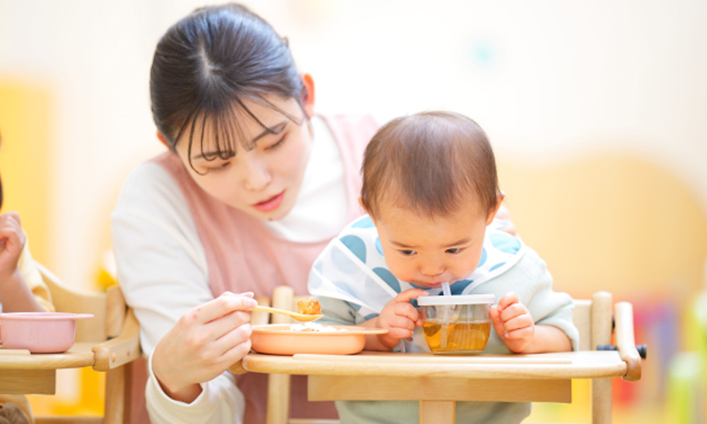 マグのお茶を飲む子供とスプーンをもっている女性のイメージ