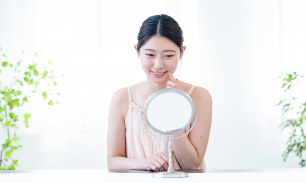 鏡を見て、笑顔の自分を確認する健康的な女性のイメージ