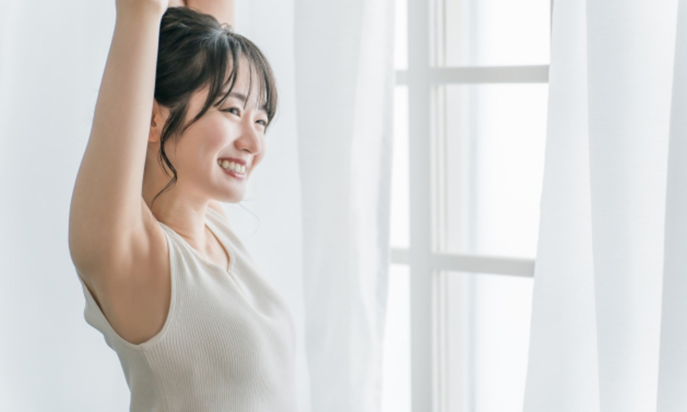 寝起きにカーテンの前で朝日を浴びる健康的な女性のイメージ