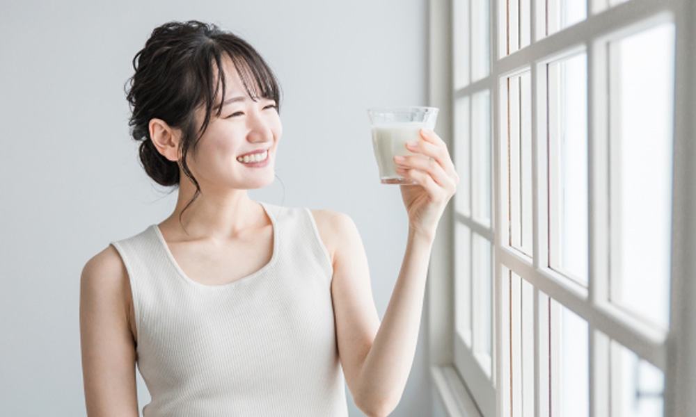家で朝アーモンドミルクを飲む健康的な女性のイメージ